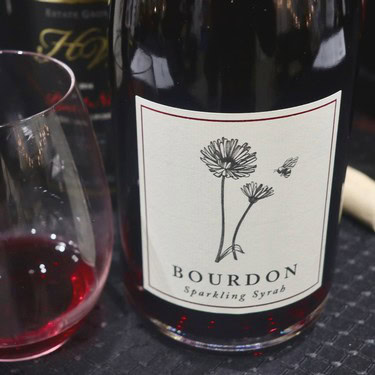 Bourdon Sparkling Syrab wine bottle with a minimalist floral label and a glass of red wine nearby.