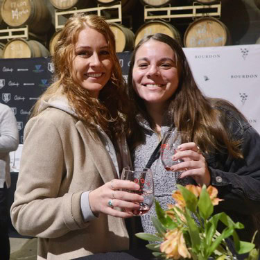 Two women enjoying wine at a Lodi Winegrape Commission event, smiling and holding glasses in a winery setting.
