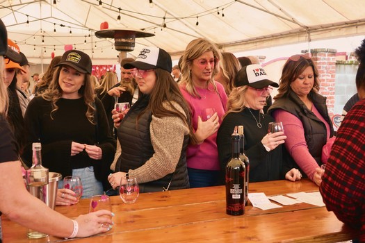 Women enjoying wine tasting at Lodi Winegrape Commission event under a tent.