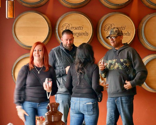 Group of people tasting wine at Lodi Winegrape Commission event in front of wine barrels.
