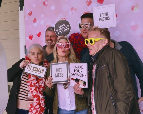 Group of five people with colorful glasses and signs at a photo booth, celebrating and having fun.