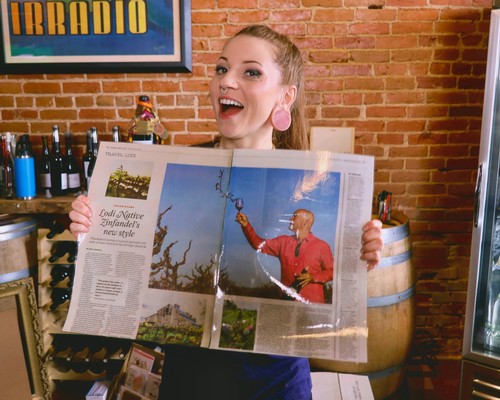 Happy woman holding a newspaper article about Lodi winegrapes in a wine shop.