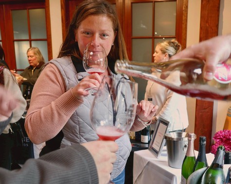 Woman tasting wine at Lodi Winegrape Commission event with others in background.