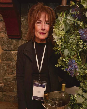 Woman at Lodi Winegrape Commission event with wine bottle and floral arrangement.