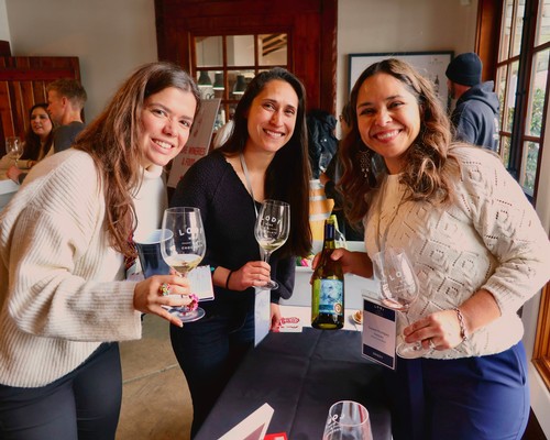 Three women smiling and holding wine glasses at a wine tasting event in Lodi, California.