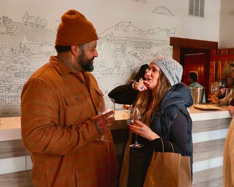 Two people enjoying wine at a Lodi Winegrape Commission event, engaging in conversation indoors.