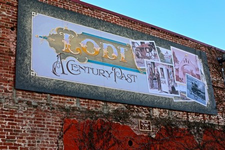 Large Lodi Winegrape Commission sign on brick wall showcasing historical images and logo.