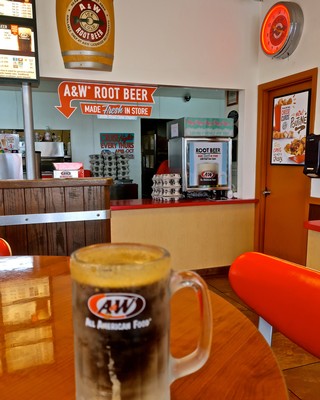 A glass of A&W Root Beer on a restaurant table with a counter in the background.