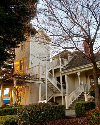 Victorian house with white exterior, wooden staircase, and leafless trees in Lodi, California.