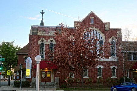 Red brick church with arched windows and a cross on top, located in Lodi, California.