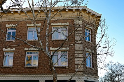 Old brick building with large windows and a leafless tree in front, under a clear blue sky.