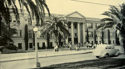 Black and white photo of the historic Lodi Winegrape Commission building with palm trees and people outside.
