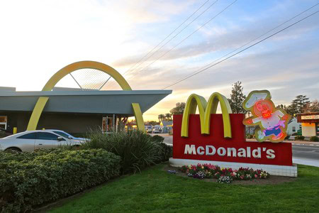 McDonald's fast food restaurant with a colorful children's play area and parking lot at sunset.