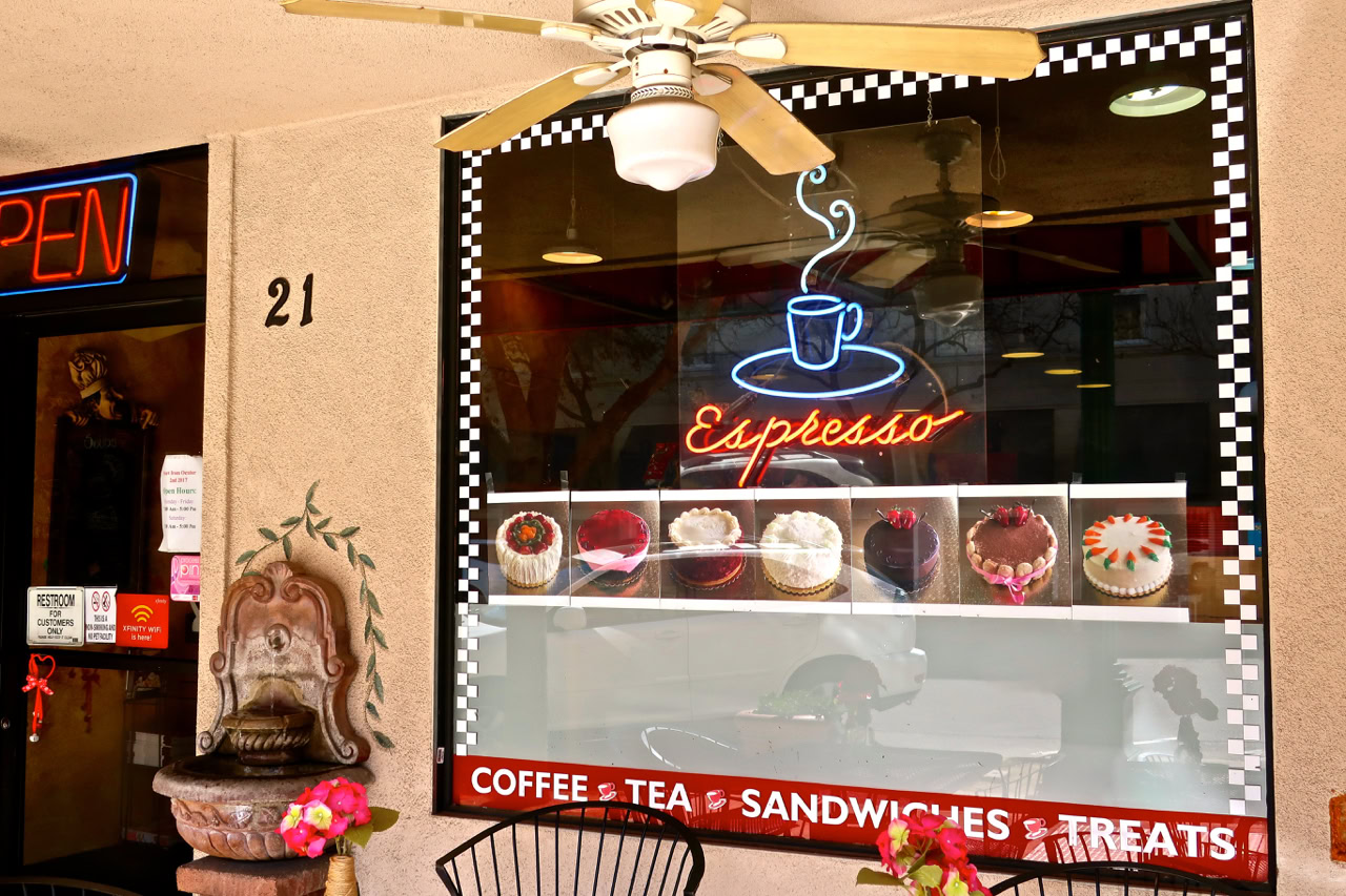 Display window of a coffee shop with cupcakes and an espresso sign, promoting local wine and treats in Lodi, California.