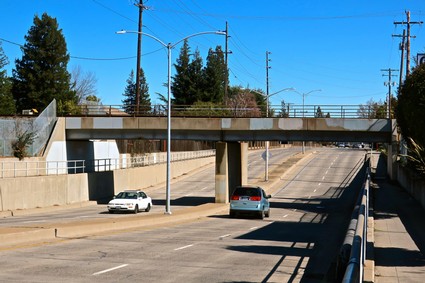 Empty road under a bridge with utility poles and trees in Lodi, California.