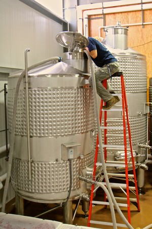 Worker inspecting stainless steel wine fermentation tanks at Lodi Winegrape Commission facility.