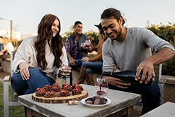 Group enjoying outdoor wine tasting with wine glasses and grapes on a sunny day.