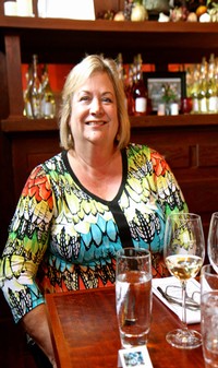 Smiling woman at a wine tasting event with glasses of wine on the table.