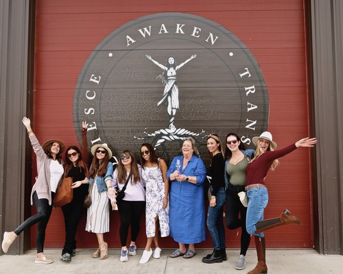 Group of women and a woman in blue dress standing in front of Lodi Winegrape Commission sign.