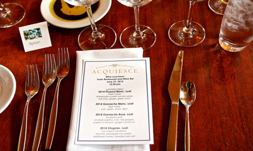Wine tasting menu at Lodi Winegrape Commission event with wine glasses and utensils on a wooden table.