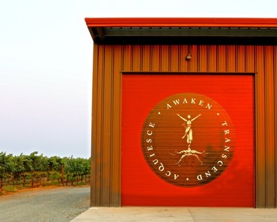 Red winery building with Lodi Winegrape Commission logo and vineyard in background.