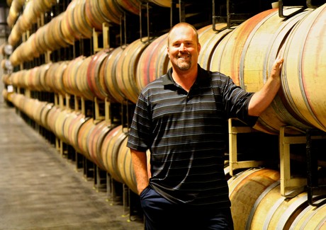 Man smiling in wine cellar with stacked wine barrels at Lodi Winegrape Commission.