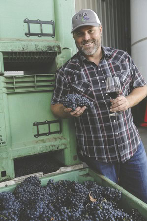 Man holding grapes and glass of wine at Lodi Winegrape Commission event.