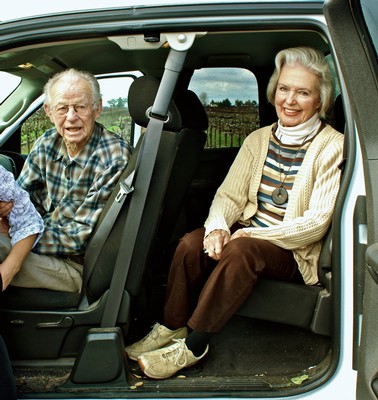 Senior couple smiling and sitting in a car, enjoying a scenic outdoor drive.
