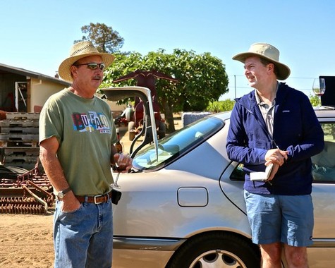 Two men in hats talking beside a car on a vineyard farm in Lodi, California.