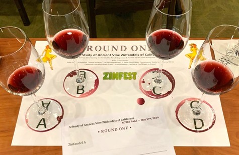 Four glasses of red wine on a tasting table with a paper sheet and wine labels from Lodi Winegrape Commission.