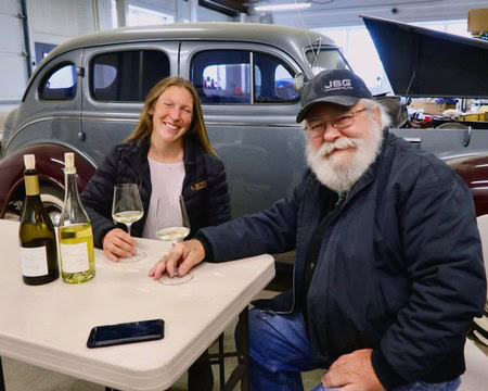 Two people enjoying wine tasting at Lodi Winegrape Commission event with vintage car in background.
