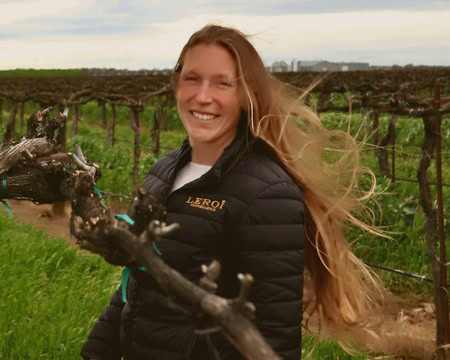 Woman smiling in vineyard with grapevines, promoting Lodi winegrapes and sustainable viticulture practices.