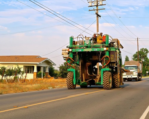 Large vineyard tractor on rural road with utility poles and houses in the background.