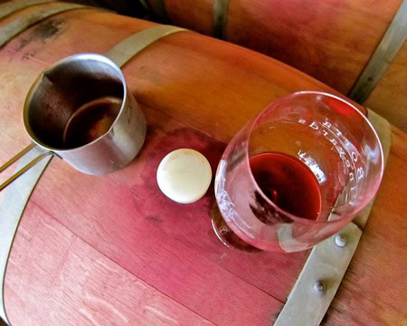 Glass of red wine on a wine barrel with a wine tasting cup and a cork.