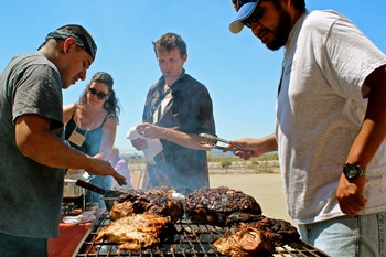 People grilling steaks outdoors on a sunny day, enjoying a barbecue gathering.