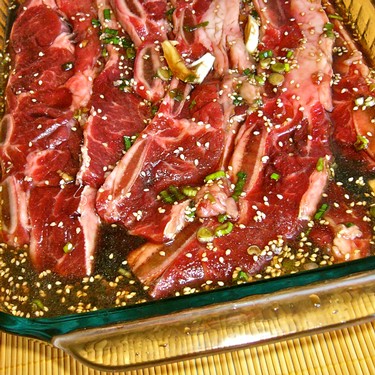 Marinated raw beef slices with herbs and sesame seeds in a glass dish.