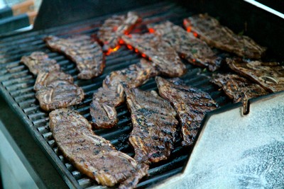 Grilled beef steaks cooking on a barbecue grill with glowing red coals.