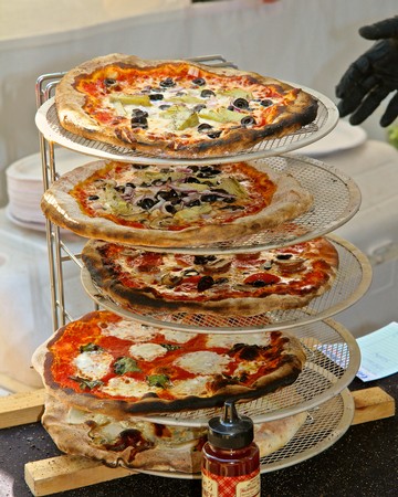 Variety of freshly baked pizzas with different toppings on a multi-tiered stand at a pizzeria.