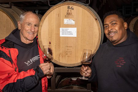 Two men tasting wine in a winery with wine barrels in the background, celebrating Lodi wine culture.