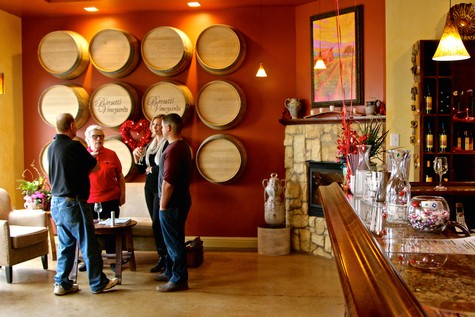 Group of people tasting wine at Lodi Winegrape Commission tasting room with barrels on wall.