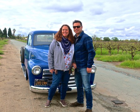 Smiling couple standing in front of vintage blue truck in Lodi wine country.