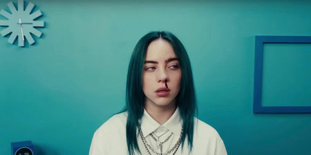 Young woman with blue hair and white shirt in a contemporary room with teal walls.