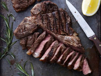 Juicy grilled steak sliced with lemon wedge and fresh herbs on a dark surface.