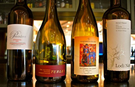Four wine bottles from Lodi Winegrape Commission showcase diverse labels and wine varieties.