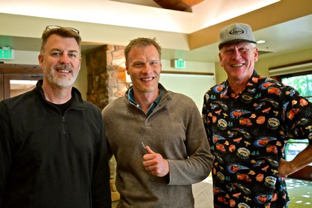 Three men smiling at a Lodi Winegrape Commission event, indoors with warm lighting and rustic decor.