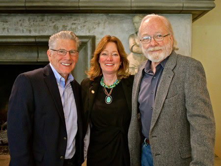 Three smiling individuals at a Lodi Winegrape Commission event, standing indoors with a fireplace in the background.