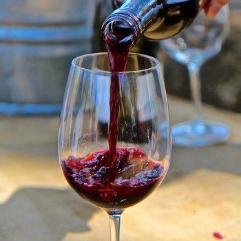 Red wine being poured into a wine glass, showcasing rich color and clarity.