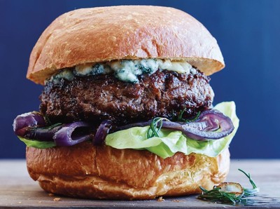 Close-up of a gourmet beef burger with blue cheese, lettuce, and purple onions on a bun.