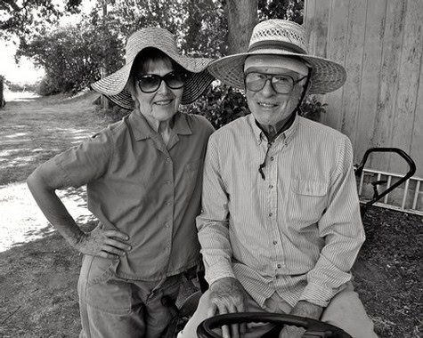 Two elderly people wearing sun hats and sunglasses outdoors, smiling at the camera.