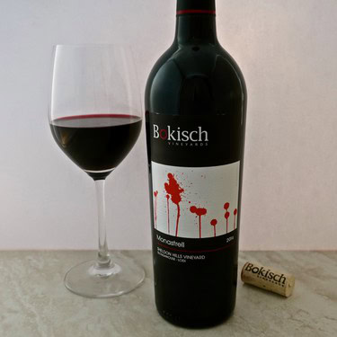 Bokisch Monastrell red wine bottle with glass of wine on a white surface.